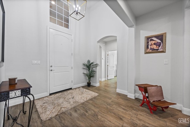 foyer with arched walkways, wood finished floors, baseboards, and a notable chandelier