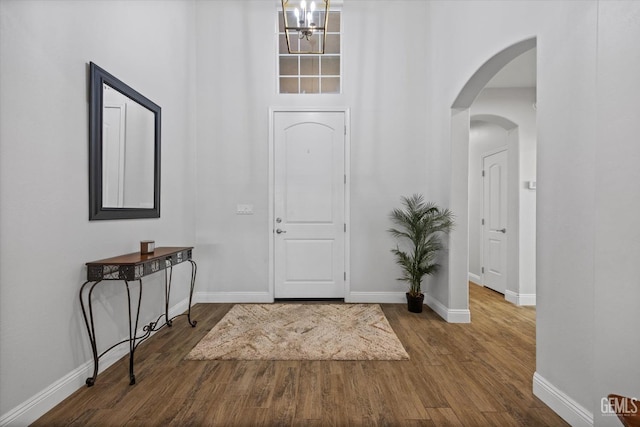 entrance foyer featuring arched walkways, baseboards, an inviting chandelier, wood finished floors, and a high ceiling