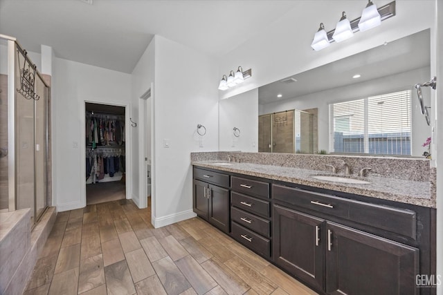 full bathroom with wood finished floors, a sink, a shower stall, and double vanity