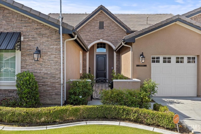 property entrance with stone siding, an attached garage, concrete driveway, and stucco siding