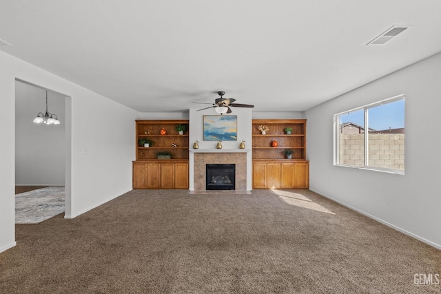 unfurnished living room with ceiling fan with notable chandelier, visible vents, carpet floors, and a tile fireplace