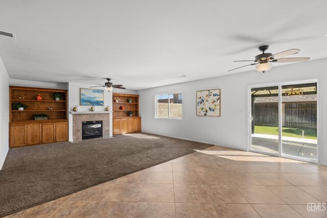 unfurnished living room featuring tile patterned floors, a tile fireplace, visible vents, ceiling fan, and carpet