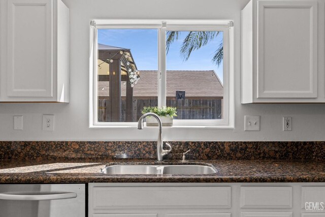 interior details featuring white cabinetry, a sink, dark stone counters, and stainless steel dishwasher