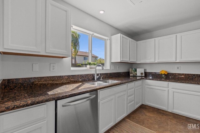 kitchen featuring stainless steel dishwasher, white cabinets, a sink, and dark stone counters