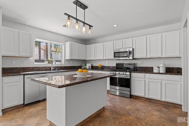 kitchen with a kitchen island, appliances with stainless steel finishes, dark stone countertops, white cabinetry, and a sink