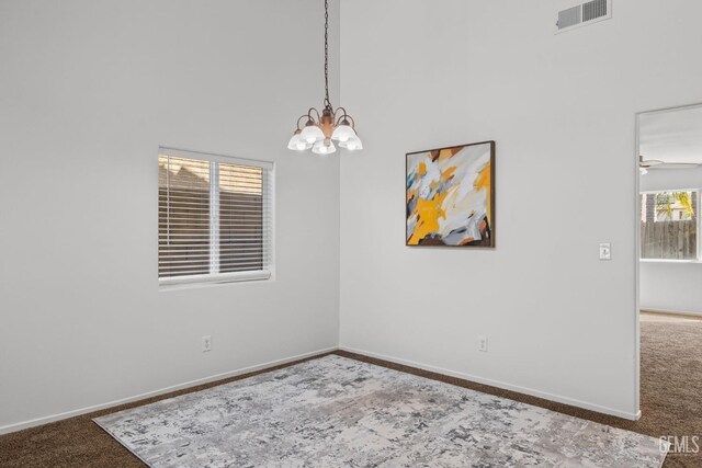carpeted empty room with baseboards, visible vents, and an inviting chandelier