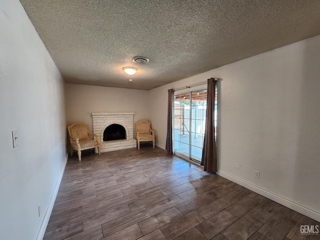 unfurnished room featuring wood-type flooring, a brick fireplace, and a textured ceiling