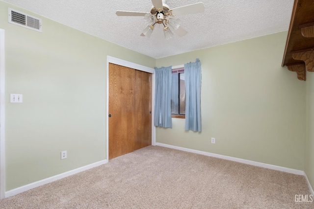 unfurnished bedroom featuring a textured ceiling, visible vents, baseboards, a closet, and carpet