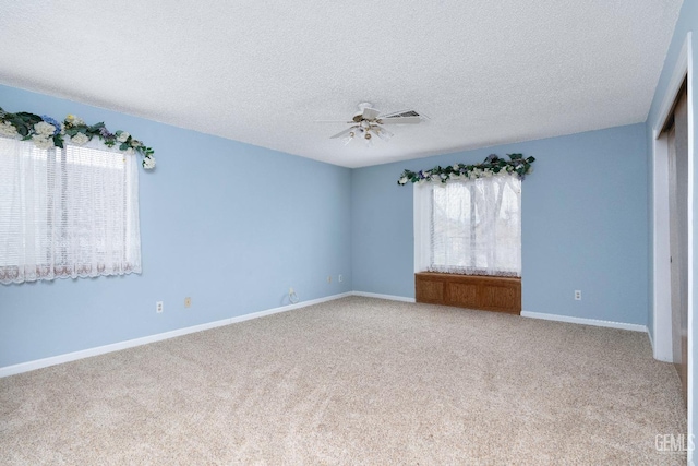 carpeted empty room with visible vents, a textured ceiling, baseboards, and a ceiling fan