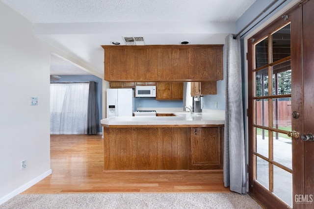 kitchen featuring a peninsula, white appliances, visible vents, and brown cabinets