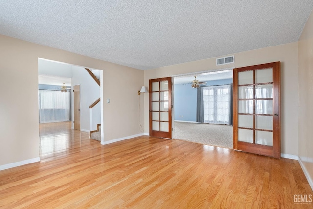 unfurnished room featuring stairway, light wood-type flooring, visible vents, and a ceiling fan