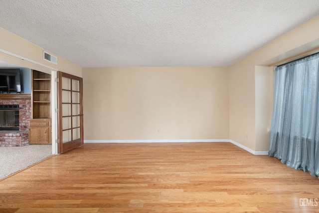 unfurnished living room featuring visible vents, light wood-style floors, a brick fireplace, a textured ceiling, and baseboards