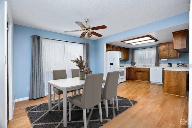 dining area featuring light wood-type flooring, ceiling fan, baseboards, and a textured ceiling