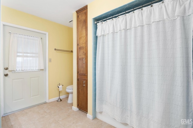 bathroom featuring toilet, shower / tub combo, tile patterned flooring, and baseboards