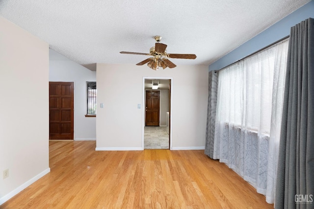 empty room featuring light wood-style flooring, baseboards, ceiling fan, and a textured ceiling