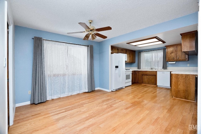 kitchen featuring white appliances, baseboards, brown cabinetry, light wood-style flooring, and light countertops