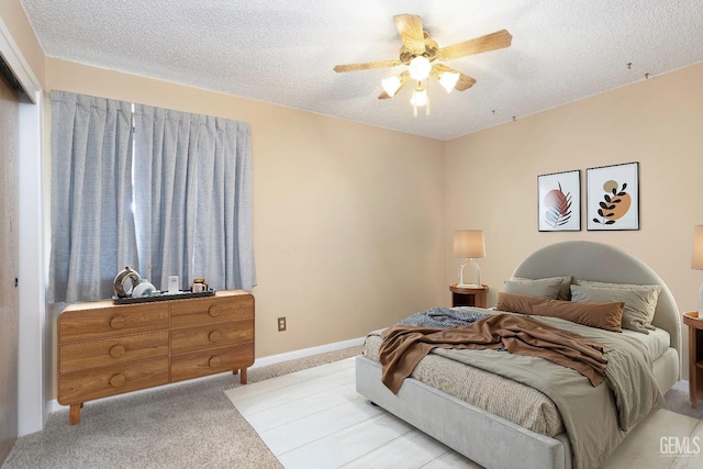 bedroom featuring light carpet, ceiling fan, baseboards, and a textured ceiling