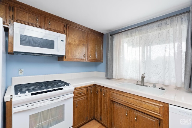 kitchen featuring tile countertops, white appliances, brown cabinetry, and a sink