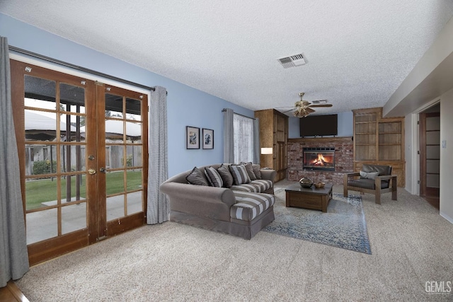 carpeted living room featuring french doors, a fireplace, visible vents, ceiling fan, and a textured ceiling