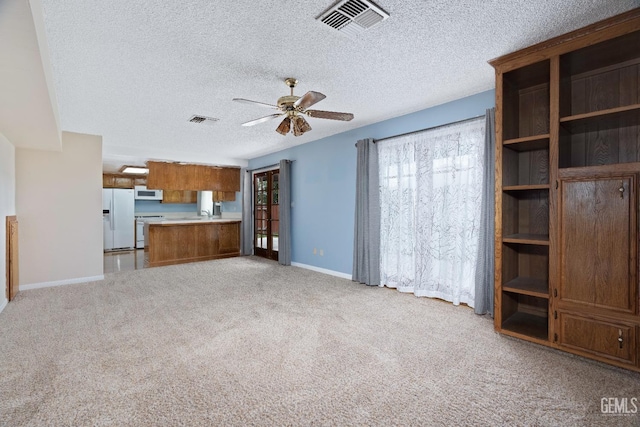 unfurnished living room featuring light carpet, plenty of natural light, visible vents, and a ceiling fan