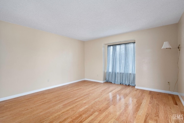 empty room featuring light wood-style flooring, baseboards, and a textured ceiling