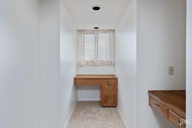 corridor with light carpet, baseboards, and a textured ceiling