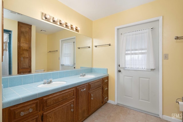 bathroom featuring tile patterned floors, a sink, baseboards, and double vanity