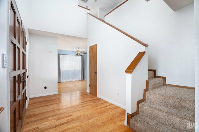 interior space with ceiling fan, wood finished floors, a towering ceiling, and baseboards