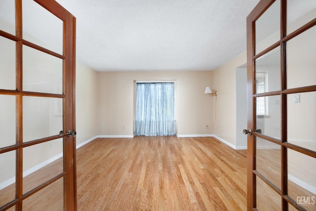 spare room featuring a textured ceiling, french doors, light wood-style flooring, and baseboards