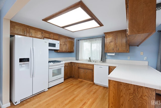 kitchen featuring light countertops, white appliances, light wood-type flooring, and brown cabinets