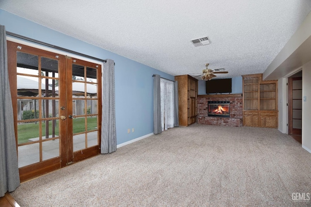 unfurnished living room featuring a textured ceiling, visible vents, french doors, a brick fireplace, and carpet