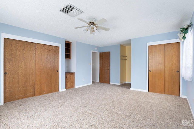 unfurnished bedroom featuring carpet floors, a textured ceiling, visible vents, and multiple closets