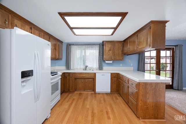 kitchen with brown cabinets, light countertops, a sink, white appliances, and a peninsula