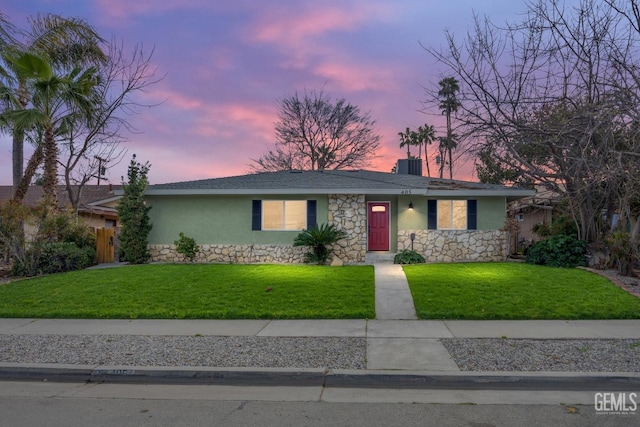 single story home featuring stone siding, a front yard, fence, and stucco siding