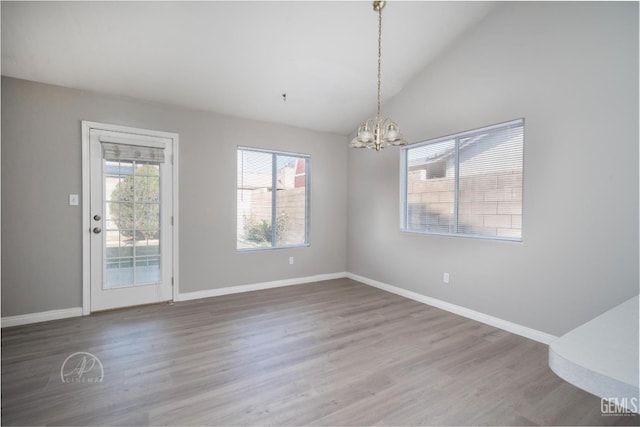 unfurnished dining area with vaulted ceiling, an inviting chandelier, and wood-type flooring