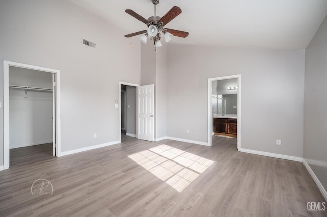 unfurnished bedroom with ensuite bathroom, a spacious closet, light hardwood / wood-style floors, a closet, and ceiling fan