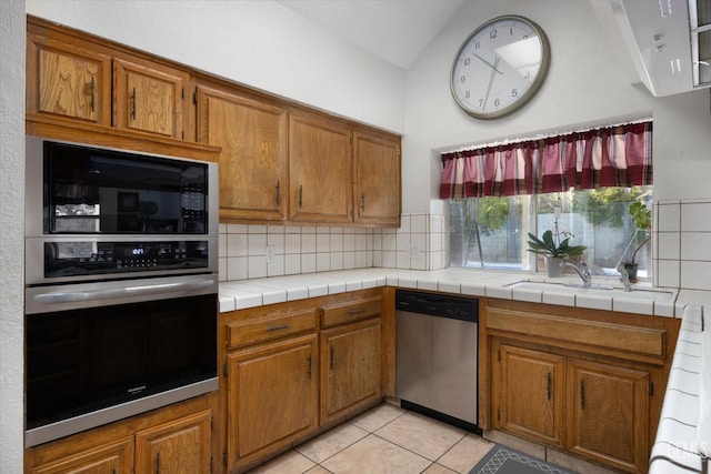 kitchen with appliances with stainless steel finishes, tasteful backsplash, lofted ceiling, tile counters, and light tile patterned floors