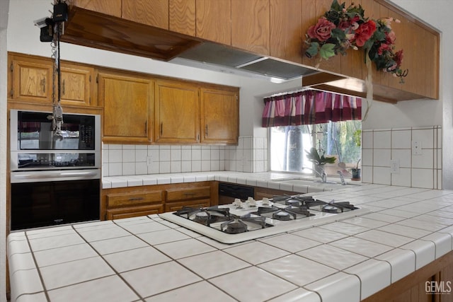 kitchen featuring tile countertops, black microwave, backsplash, stainless steel oven, and white gas cooktop