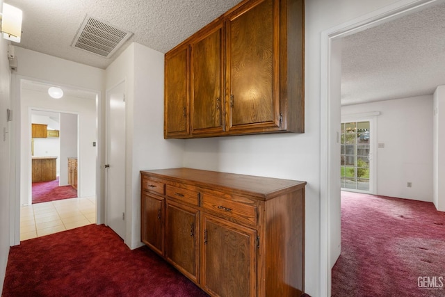 hall with tile patterned floors, visible vents, carpet flooring, and a textured ceiling