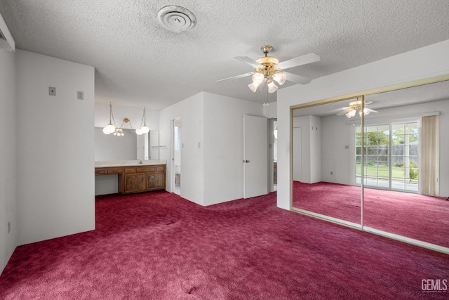 unfurnished bedroom featuring connected bathroom, dark carpet, a closet, a textured ceiling, and access to outside