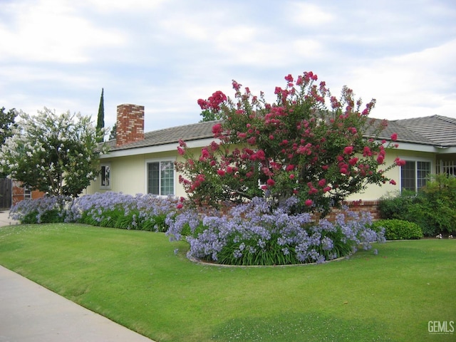 view of side of property with a yard, a chimney, and stucco siding