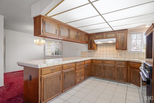 kitchen with a peninsula, brown cabinets, under cabinet range hood, and oven