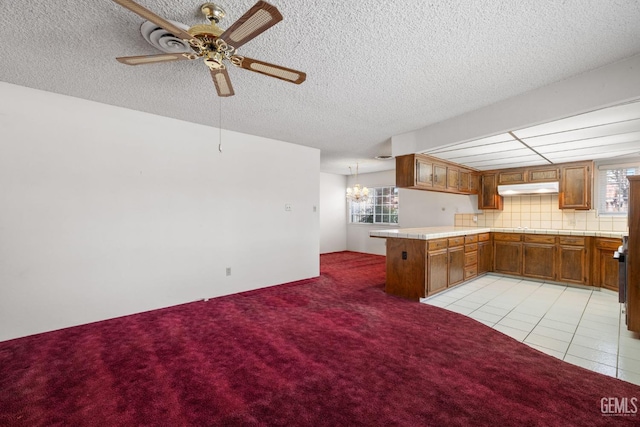 kitchen with under cabinet range hood, light colored carpet, a peninsula, brown cabinetry, and a ceiling fan