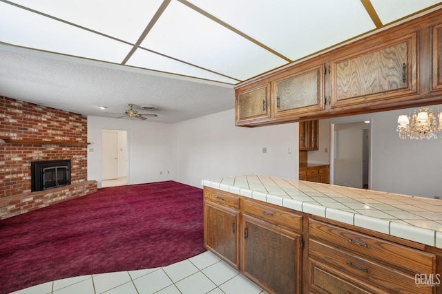 kitchen featuring brown cabinets, a textured ceiling, a brick fireplace, ceiling fan with notable chandelier, and open floor plan