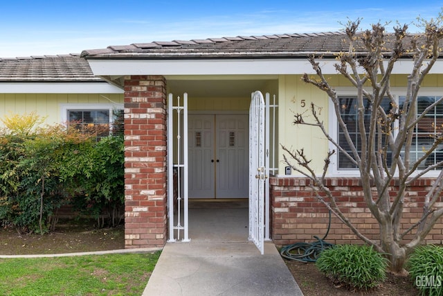 view of exterior entry featuring brick siding and a tile roof