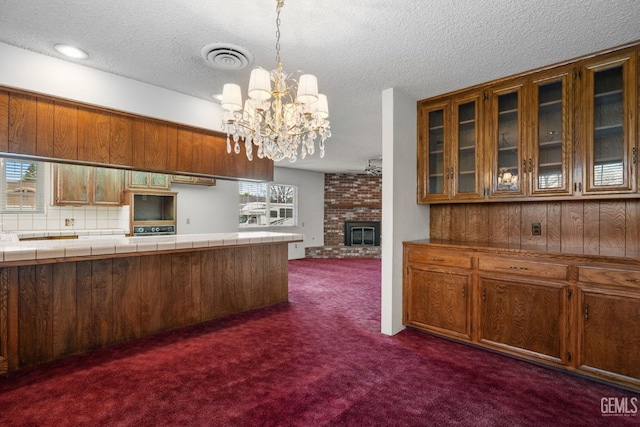 kitchen with visible vents, tile counters, a fireplace, brown cabinetry, and dark colored carpet