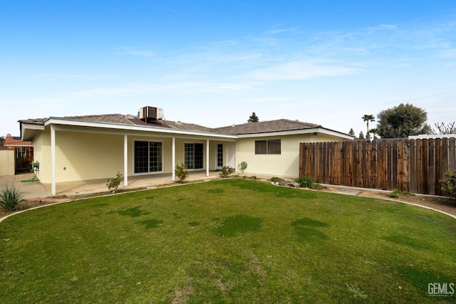 rear view of house with fence, stucco siding, cooling unit, a lawn, and a patio