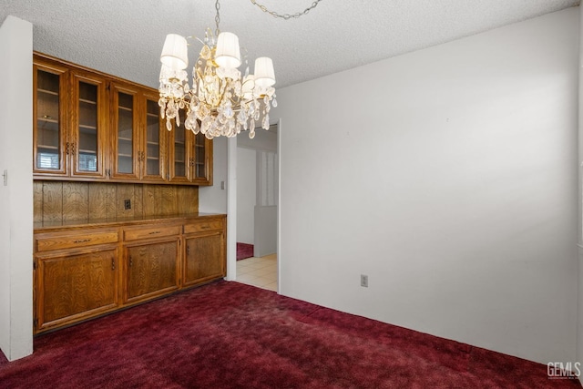 unfurnished dining area with carpet flooring, a textured ceiling, and an inviting chandelier