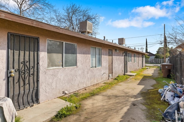 view of property exterior featuring stucco siding, central AC, and fence