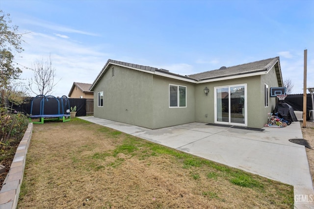 back of property featuring a patio area, a trampoline, and a lawn